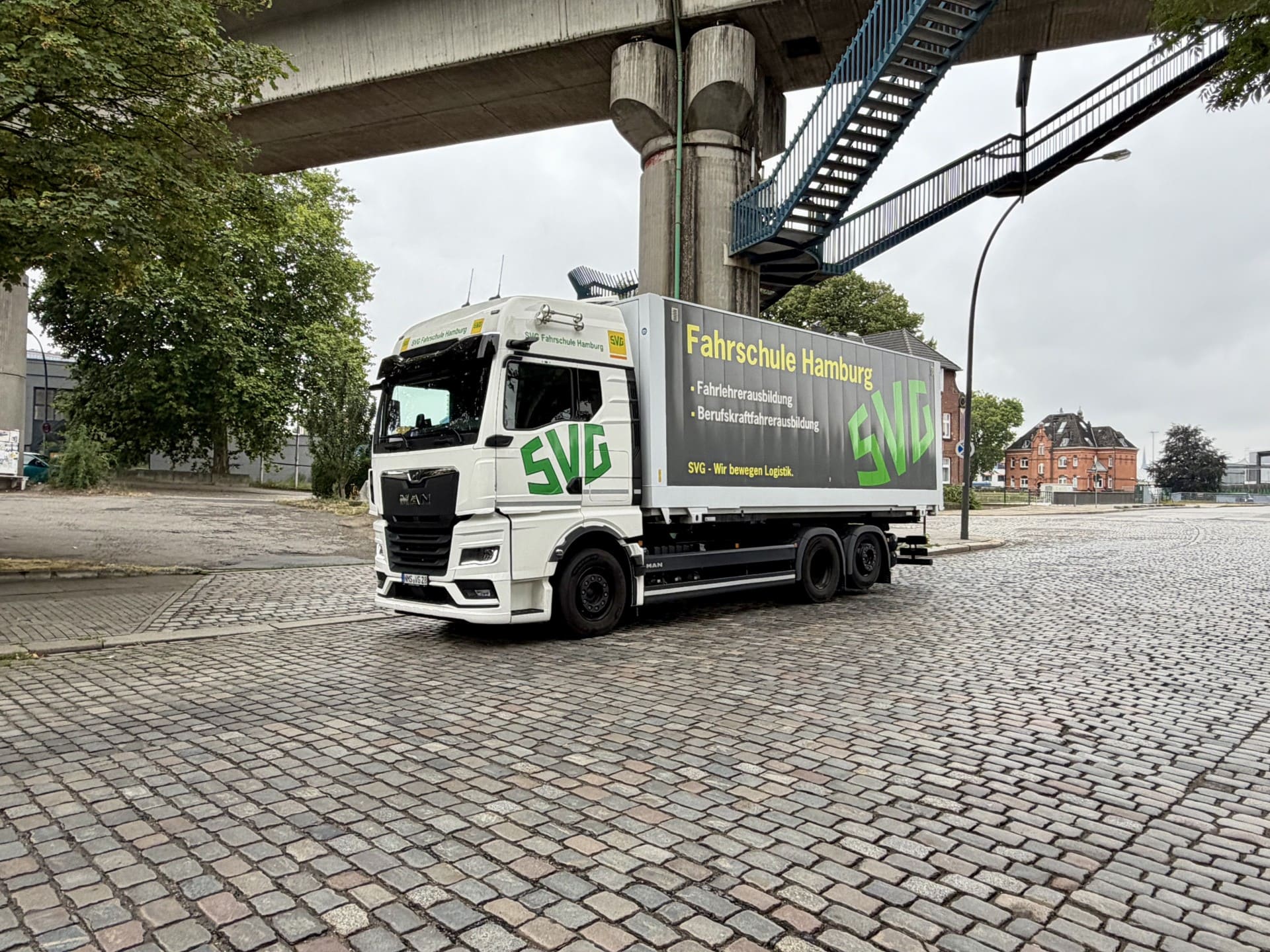 Weisser MAN Fahrschul LKW der SVG Hamburg auf Kopfsteinpflaster unter einer Bruecke